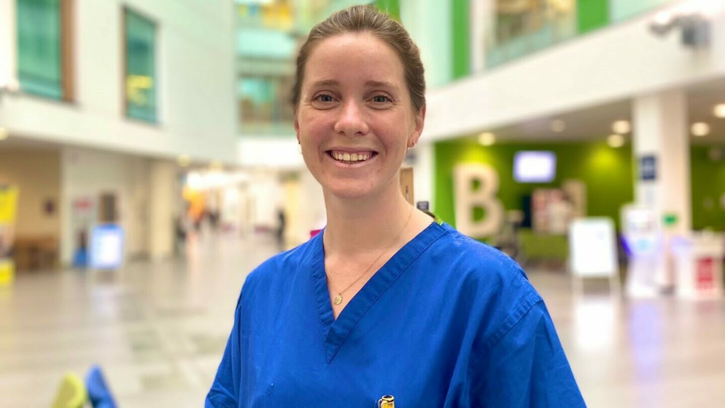 Dr Rachel Scott, co-founder of Bleep101, is wearing blue scrubs and standing in Southmead Hospital's Brunel Building
